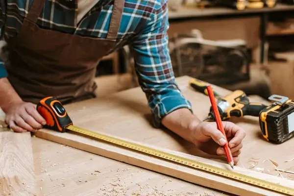 Carpenter measuring wood for minor carpentry and trim repairs by a painter in Clovis, CA.